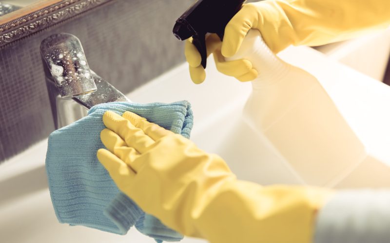 Cropped image of beautiful young woman using a duster and a detergent while cleaning sink and tap in bathroom